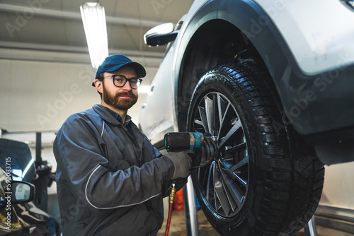 medium shot of a car mechanic changing a car wheel tire with a pneumatic wrench in auto service. High quality photo © PoppyPix