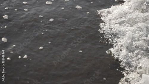 Close up of shallow ocean water in slow motion. Volcanic sand can be seen below the water.