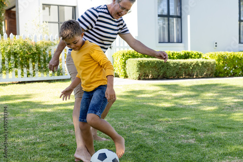 Cheerful caucasian grandfather and grandson playing soccer on grassy field in yard, copy space photo