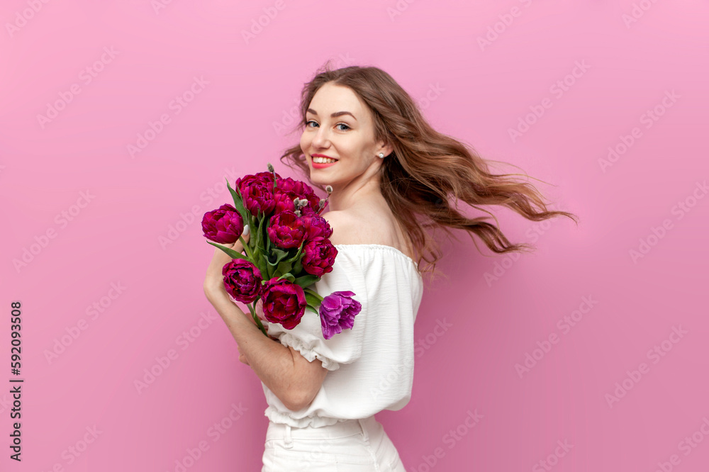 young attractive girl in white clothes holds bouquet of pink tulips and smiles, woman on holiday with flowers