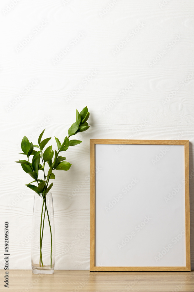 Vertical of empty wooden frame with copy space and plant on table against white wall Vertical of empty wooden frame with copy space and plant on table against white wall