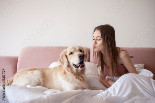 girl lies in bed and hugs golden retriever dog, the dog licks the owner, the woman loves pets