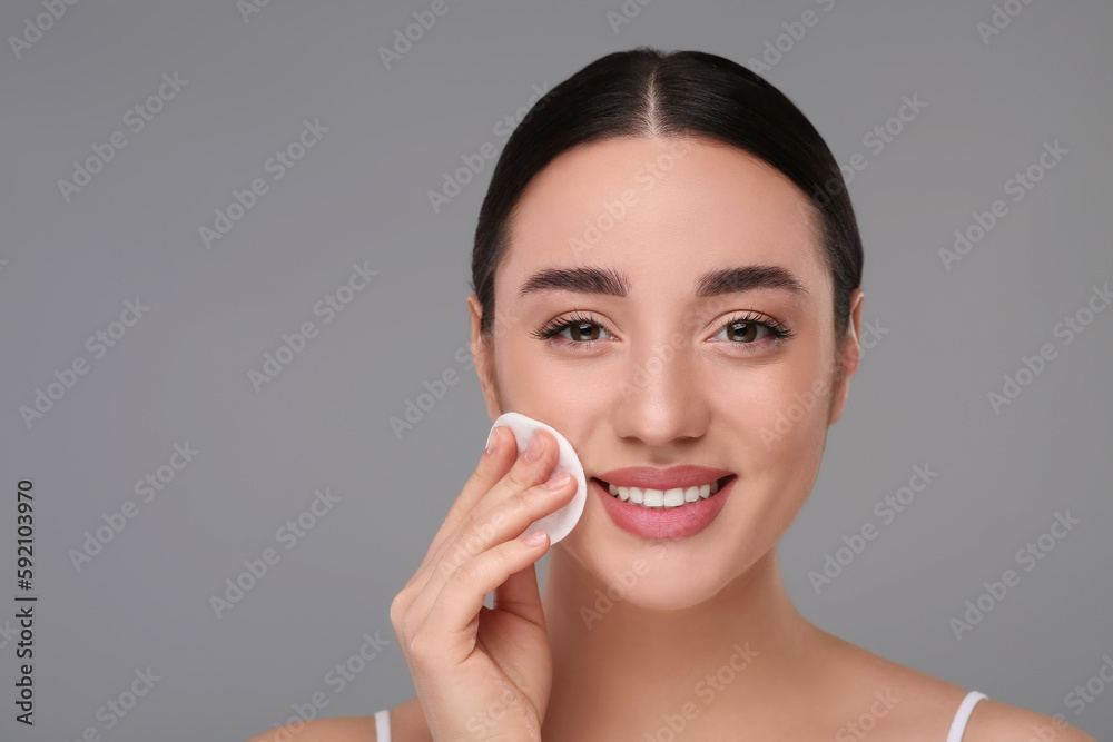 Beautiful woman removing makeup with cotton pad on gray background, space for text Beautiful woman removing makeup with cotton pad on gray background, space for text