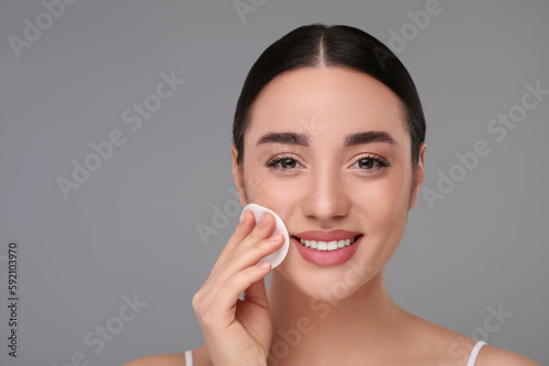 Beautiful woman removing makeup with cotton pad on gray background, space for text