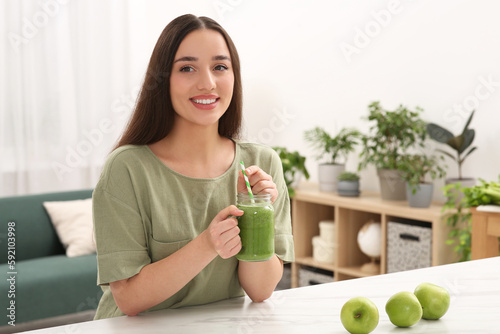 Beautiful young woman with mason jar of delicious smoothie and apples at home
