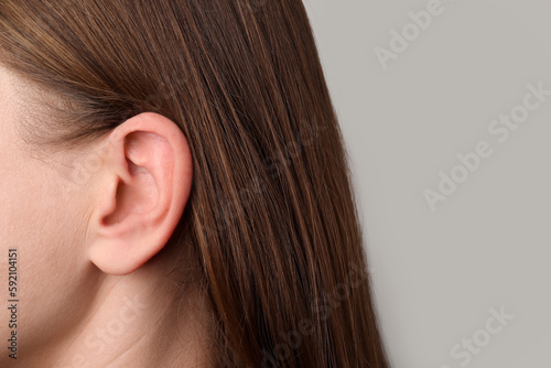 Closeup view of woman against light grey background, focus on ear