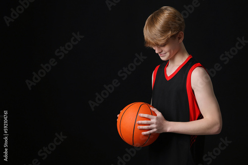 Teenage boy with basketball ball on black background. Space for text