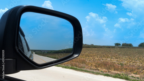 Car on the concrete road drive to nature. Travel to clear the province. Beside road with agricultural area of the seedlings of pineapple plantation under blue sky. Focus to mirror view backside.