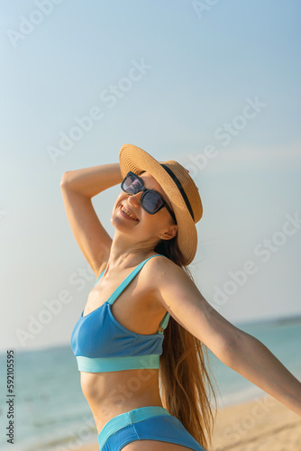 Beautiful caucasian blonde woman in bikini with beach hat and sunglasses wandering by the beach © asean studio