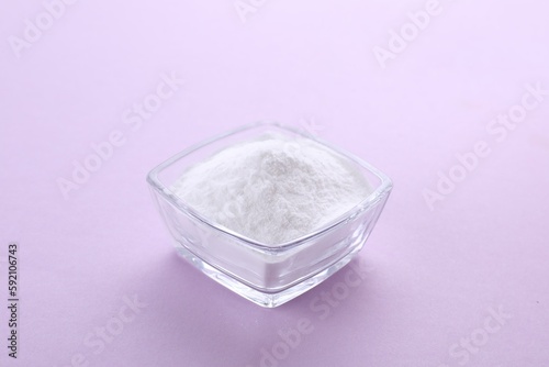 Bowl of sweet powdered fructose on light purple background
