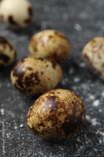 Many speckled quail eggs on black textured table, closeup