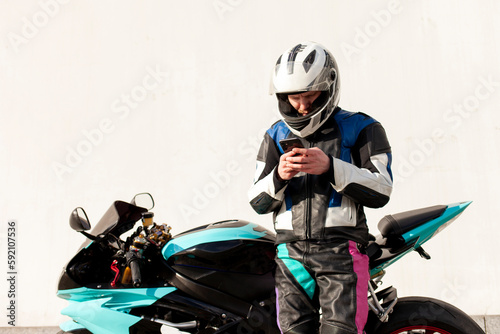 guy motorcyclist in professional protective equipment and helmet sits on sports motorcycle and uses smartphone