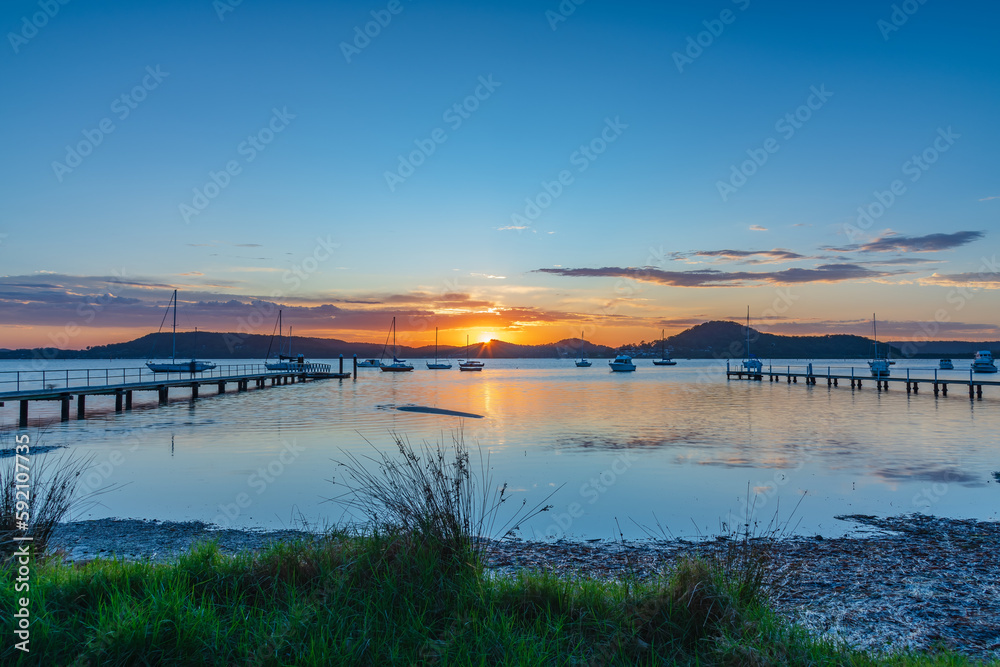 Sunrise waterscape with boats, wharves and sun coming over the mountain range