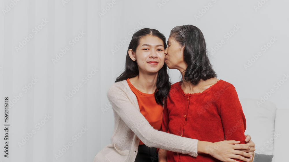 Kiss, Senior mature asian woman with young daughter sitting together on couch, giving hug and love feeling happy, Mother day, birthday, family anniversary, love mom concept. Kiss, Senior mature asian woman with young daughter sitting together on couch, giving hug and love feeling happy, Mother day, birthday, family anniversary, love mom concept.