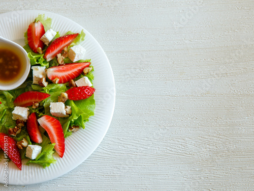 Plate of homemade fresh summer sliced Strawberry and lettuce salad with feta cheese and walnuts. Organic healthy diet, vegetarian salad food. Top view, copy space