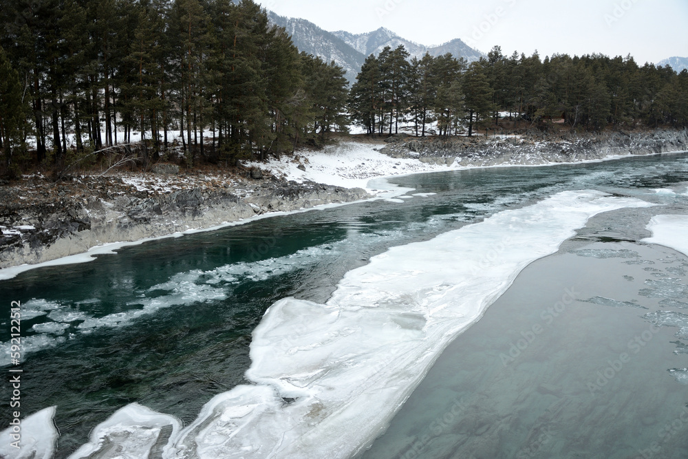 Huge pieces of ice on the thawed bed of a beautiful river flowing through a forested valley in the early winter morning. Huge pieces of ice on the thawed bed of a beautiful river flowing through a forested valley in the early winter morning.
