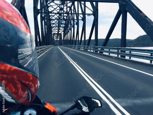 Passenger's view of a motorcyclist with a red helmet riding over a steel bridge over a river