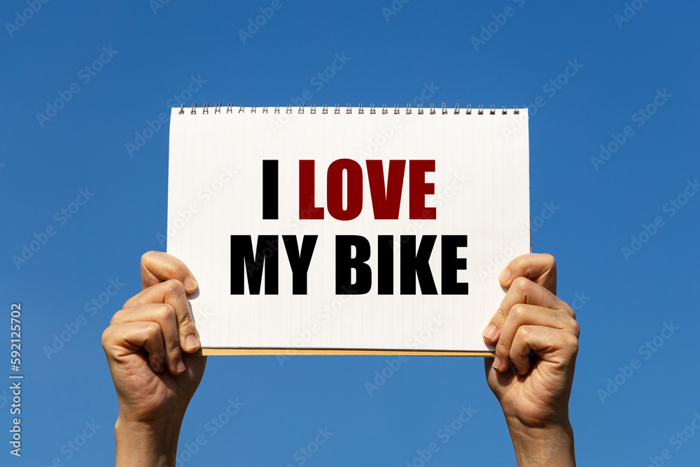 I love my bike text on notebook paper held by 2 hands with isolated blue sky background. This message can be used as business concept about my bike. I love my bike text on notebook paper held by 2 hands with isolated blue sky background. This message can be used as business concept about my bike.
