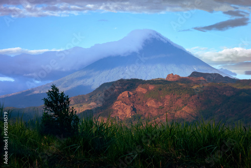 Panoramic view in rural area and in the background volcano called Agua in Guatemala covered with clouds and illuminated by sunlight at sunset.