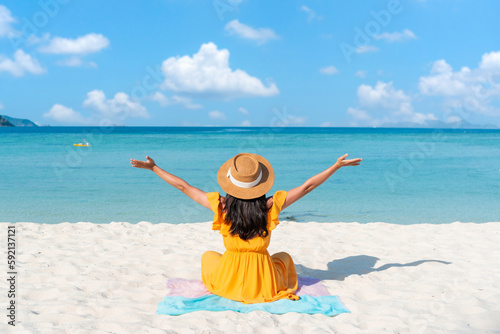 Carefree young Asian traveler female relaxing at tropical sandy beach with beautiful blue sky. Summer vacation concept. Copy space photo