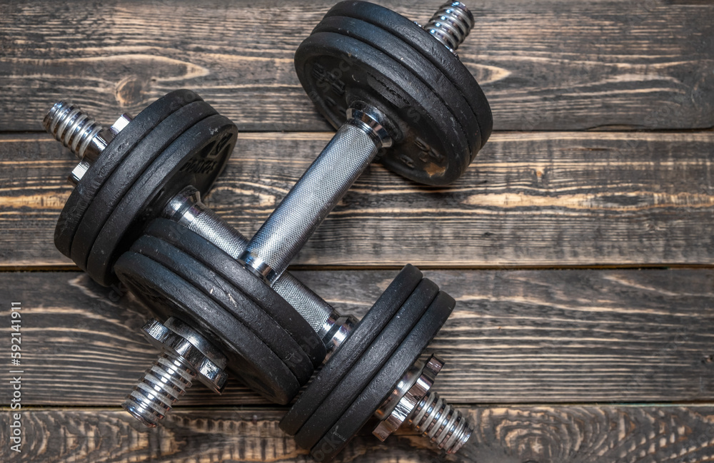 Naklejka premium Iron dumbbells with metal pancakes on a wooden background.