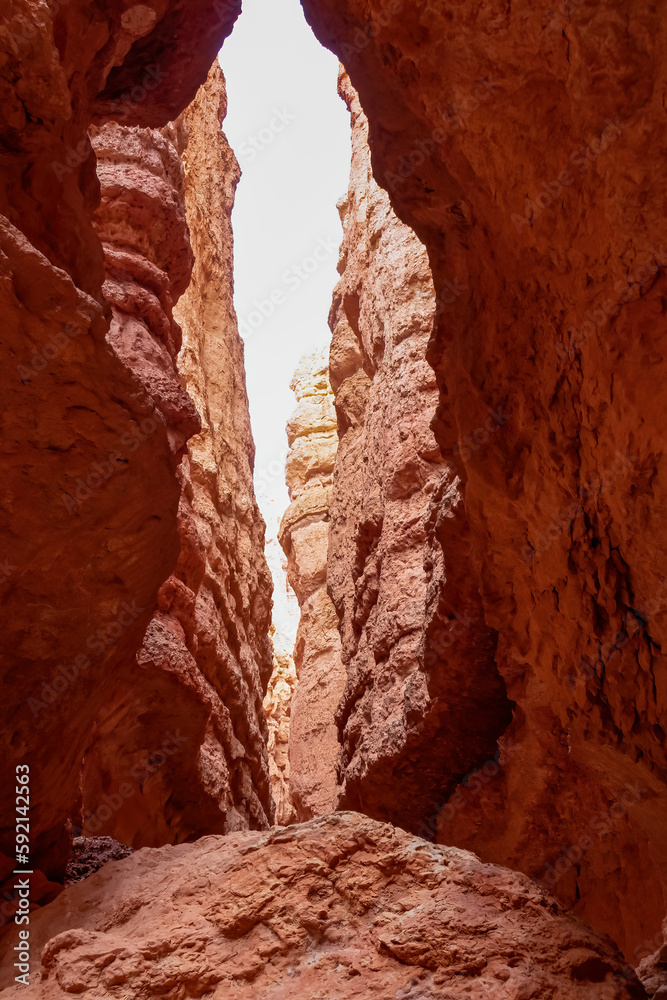 Narrow Navajo hiking trail through massive cliffs of hoodoo sandstone rock formation in Bryce Canyon National Park, Utah, USA. Barren desert landscape with view of natural amphitheatre in summer