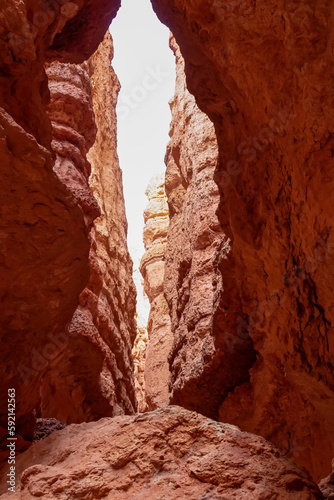 Narrow Navajo hiking trail through massive cliffs of hoodoo sandstone rock formation in Bryce Canyon National Park, Utah, USA. Barren desert landscape with view of natural amphitheatre in summer