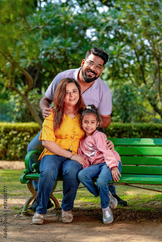 Happy Young indian parents with their cute little daughter sitting at park or garden.