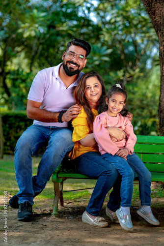 Happy Young indian parents with their cute little daughter sitting at park or garden. © Niks Ads