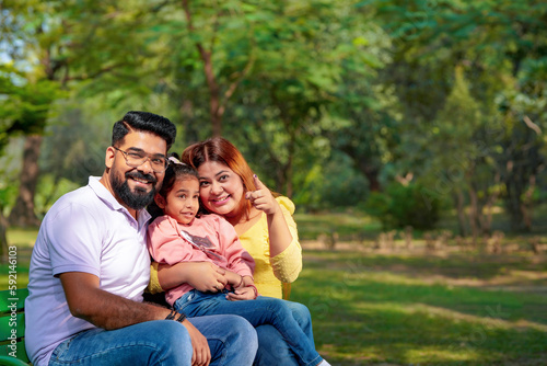 Happy Young indian parents with their cute little daughter sitting at park or garden.