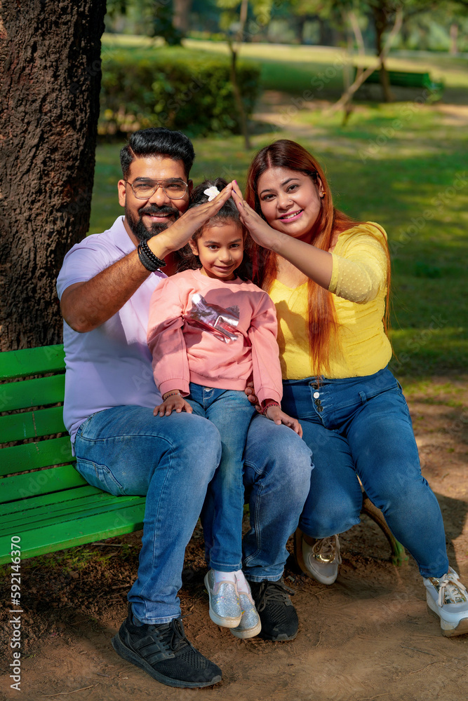 Happy Young indian parents with their cute little daughter sitting at park or garden. Happy Young indian parents with their cute little daughter sitting at park or garden.