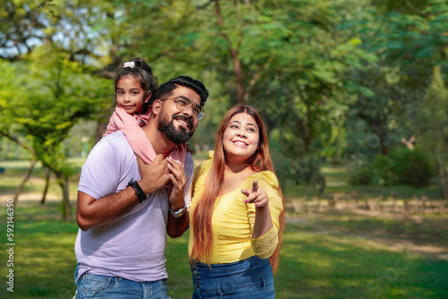 Happy Young indian parents with their cute little daughter sitting at park or garden. © Niks Ads