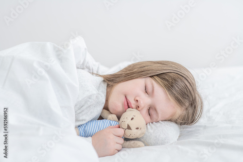 Happy little girl sleeps with toy bear on the bed at home