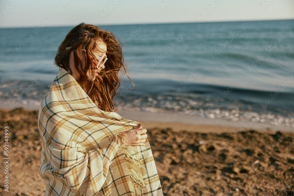 a woman in large glasses wraps herself in a blanket walking along the sea coast a woman in large glasses wraps herself in a blanket walking along the sea coast