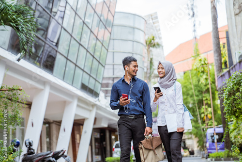 Asian male and female Muslim workers chat while walking to work together between office buildings in the city © Odua Images