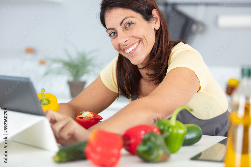 woman cooking with peppers and using tablet