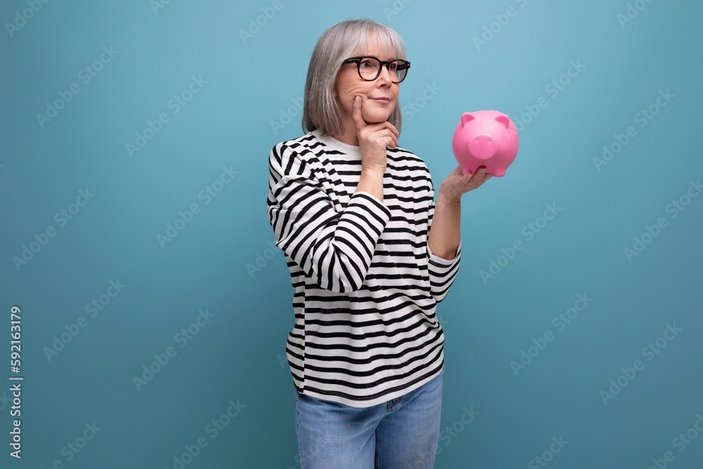 ingenious grandmother middle-aged woman has an idea where to invest her savings from a piggy bank on a bright background with save space - obrazy, fototapety, plakaty 