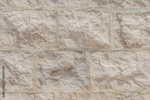 Light cream texture of the wall surface, built of rectangular natural bricks with even seams between them. Real rough surface of stone blocks of delicate color