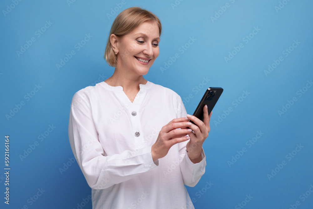 pensive slender blondie middle-aged woman in a white blouse masters the smartphone gadget pensive slender blondie middle-aged woman in a white blouse masters the smartphone gadget