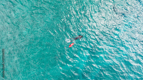 Free diver spearfishing with a red safety buoy in the middle of the ocean sea in Hawaii. Aerial top-down drone view.