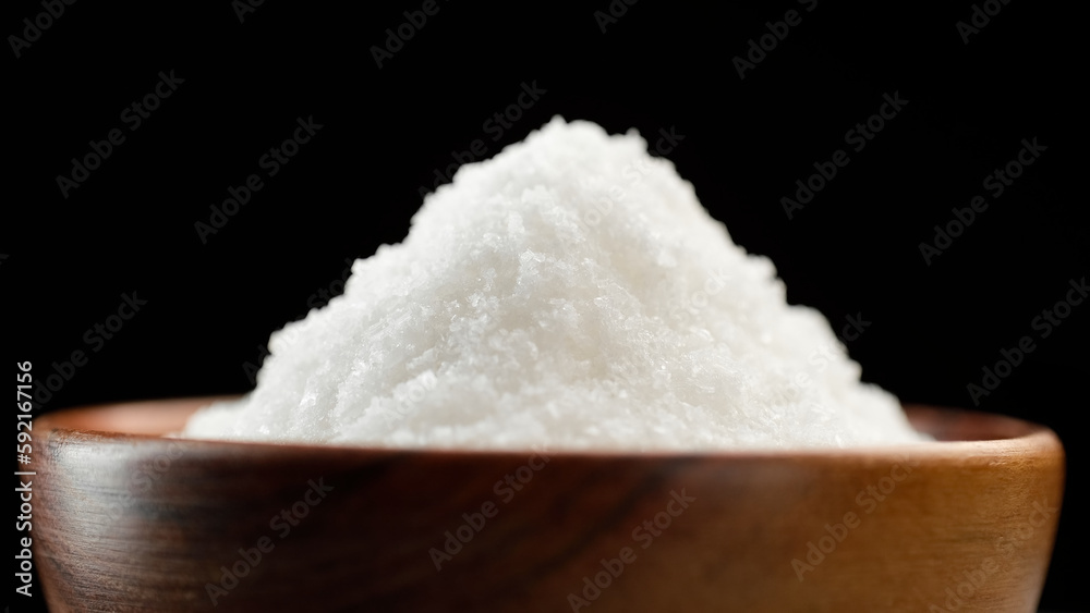 White table salt falling in wooden bowl, close up