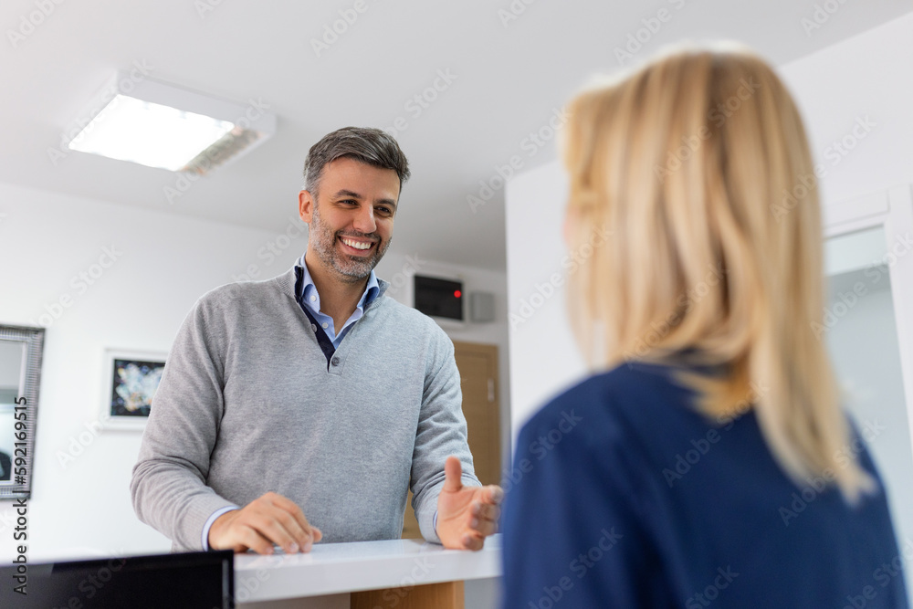 Man making an appointment with medical staffs at reception desk in hospital. Medical staff and nurse - receptionist talking to patient in front of the reception counter in hospital. - obrazy, fototapety, plakaty 