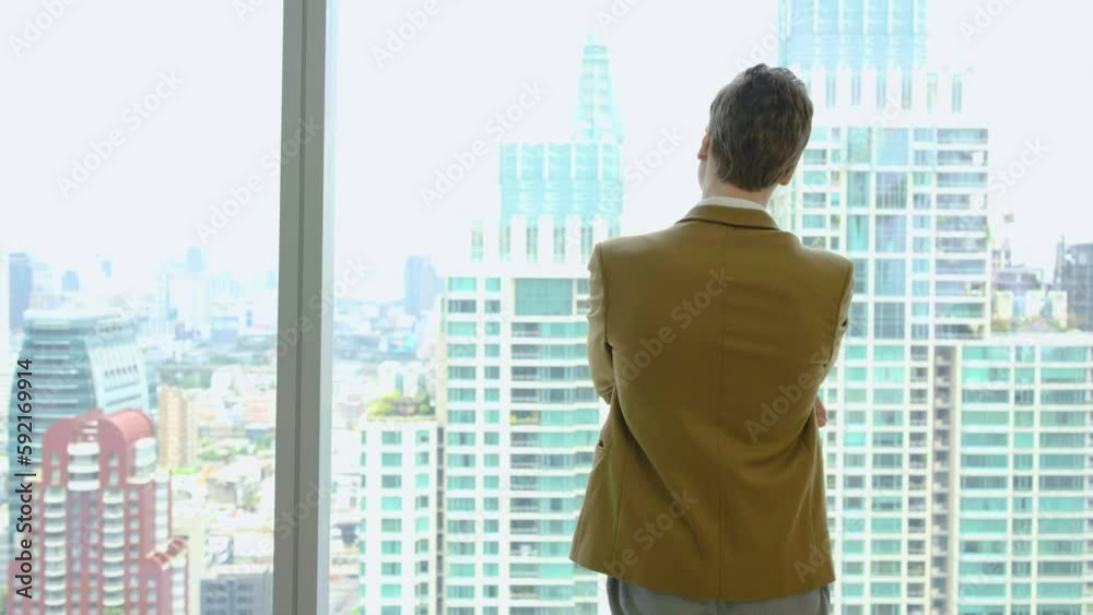 Back View of the Thoughtful Businessman wearing a Suit Standing in Office, Contemplating Big Business Deal, Looking out of the Window, planning ahead thinking of ideas for future investment strategy Back View of the Thoughtful Businessman wearing a Suit Standing in Office, Contemplating Big Business Deal, Looking out of the Window, planning ahead thinking of ideas for future investment strategy