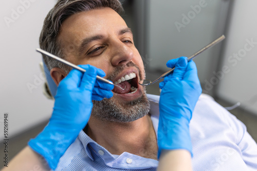 Over the shoulder view of a dentist examining a patients teeth in dental clinic. Man having his teeth examined by a young female dentist.