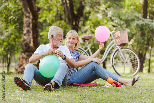 Healthy senior couple blow up colored ballons and happy smiling fun playing in plublic park sunny day. photo