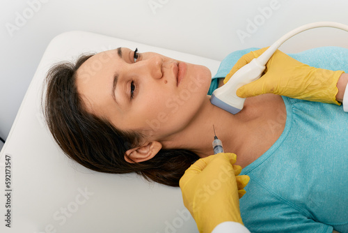 Thyroid nodule biopsy. Adult woman during fine needle aspiration biopsy guided ultrasonic and ultrasound specialist photo