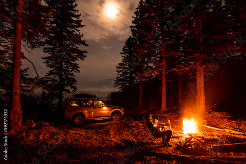 A man sitting at campfire in a tourist camp in a fir forest near the sea.