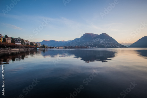 Panorama of Lugano lake and the city in autumn early morning with Swiss and Italian mountains in the background. Lugano, Ticino, Switzerland