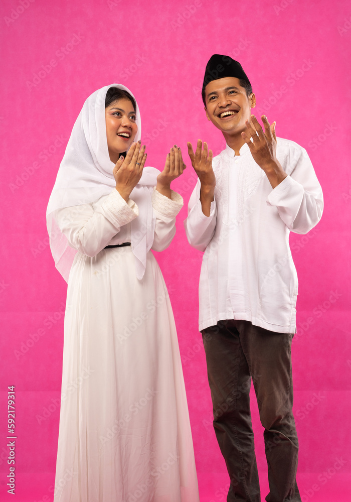 portrait of Asian Muslim couple stands with praying hand gesture on pink background portrait of Asian Muslim couple stands with praying hand gesture on pink background