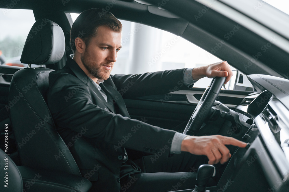 Turning the knobs. Man in formal business clothes is sitting in the modern automobile Turning the knobs. Man in formal business clothes is sitting in the modern automobile